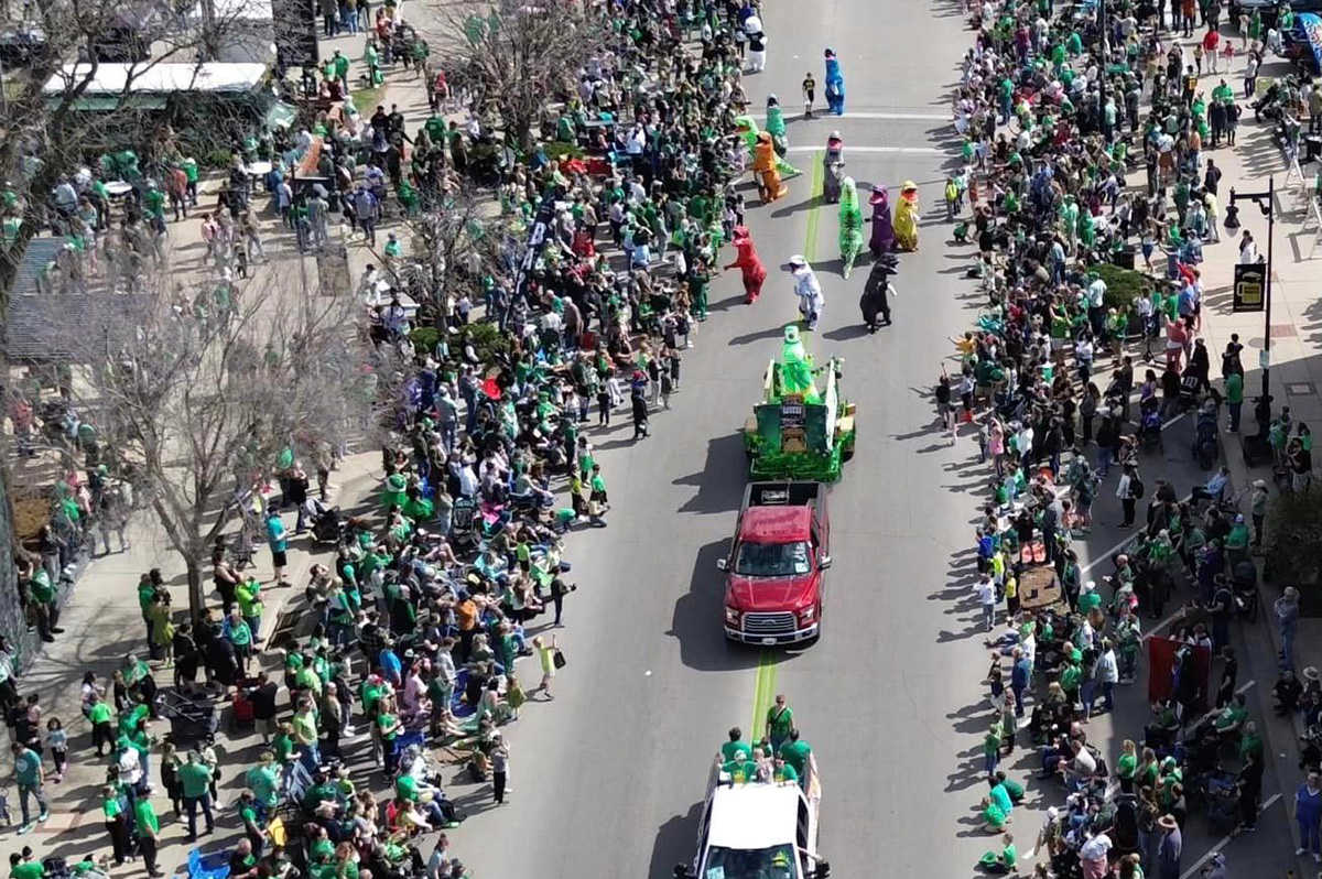 Aerial view of the Delano Paddy Day Parade featuring trucks, floats and dancing dinosaurs.