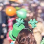 Woman wearing a shamrock headband looks out over crowded street.